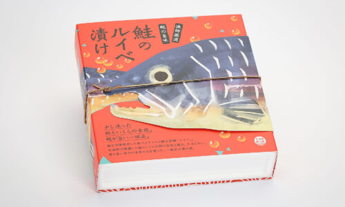 【制作実績・使用例】鮭の切り身入りの箱に巻かれた****鮭の形の特殊型抜き巻紙。マットPPとマットニスで冷凍環境に適したパッケージ外装。**